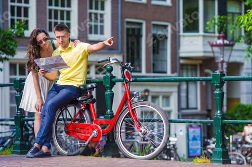 Preview: Young tourists couple looking at map with bikes in european city