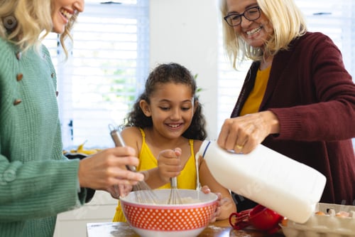 Preview: Happy multiracial multigeneration female family preparing baked food on table in kitchen