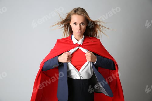 Preview: Confident businesswoman wearing superhero costume under suit on light grey background
