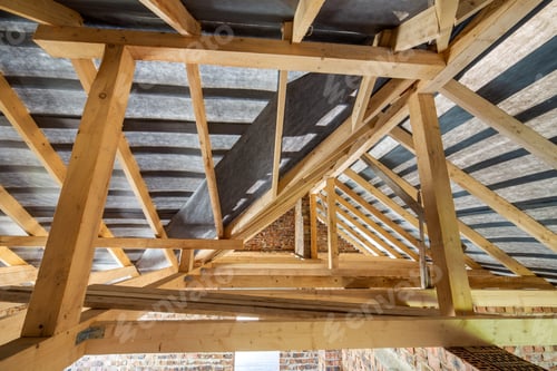 Preview: Attic of a building under construction with wooden beams of a roof structure and brick walls.