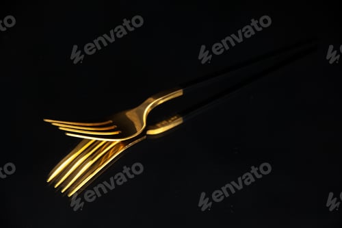 Preview: Close up view of elegant shiny golden fork on black blurred background with free space