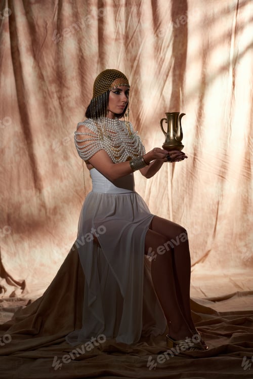 Preview: Woman in traditional egyptian outfit holding golden jug while sitting on abstract background