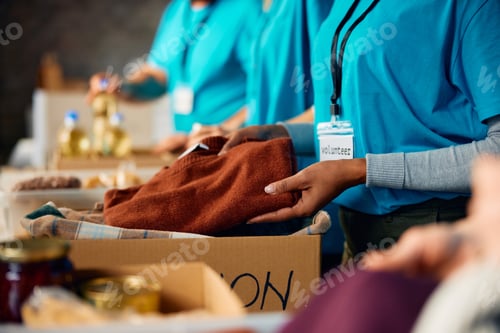 Preview: Close up of volunteer packing donated clothes into cardboard boxes at community center.