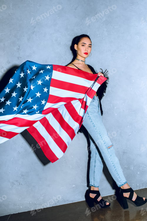 Preview: beautiful asian woman with american flag against concrete wall