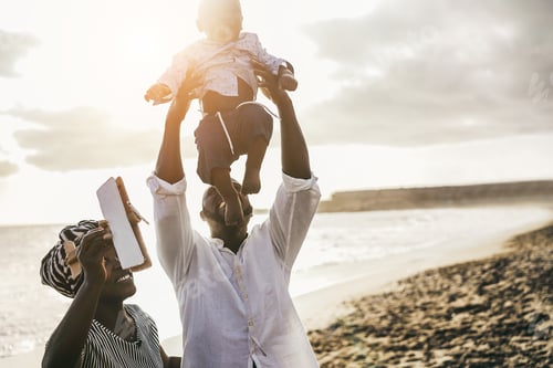 Preview: African parents and little son having fun with wood airplane on the beach