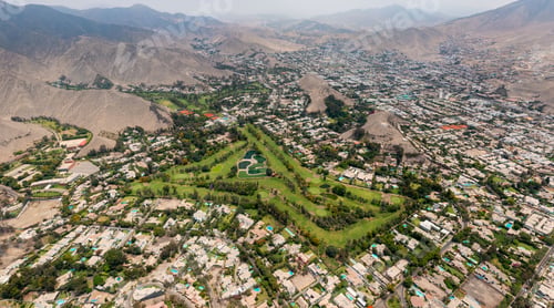 Preview: aerial photograph of the city in the middle of mountains with an open green field and