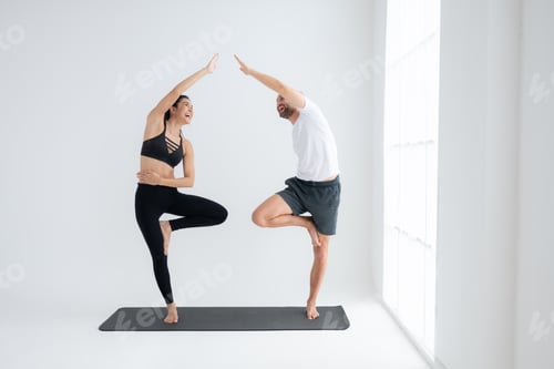 Preview: Young couple practicing yoga in a white room of studio.