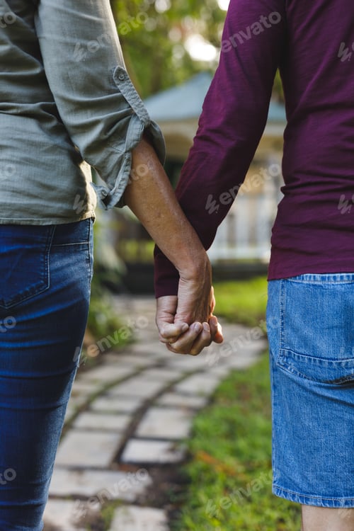 Preview: Mid section of senior caucasian couple holding hands in sunny garden