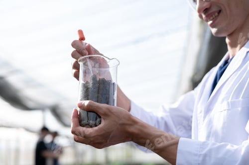 Preview: Blurred asian agricultural scientist man holding beaker testing on planting soils in greenhouse farm