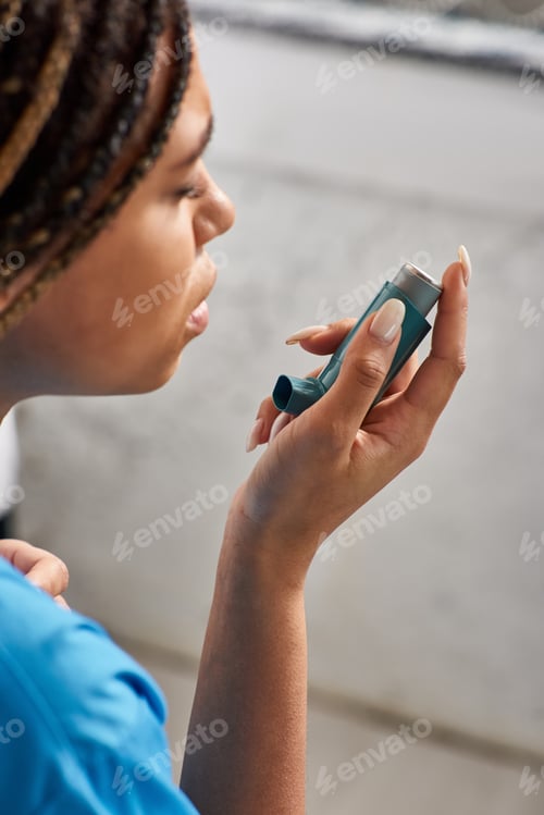 Preview: young ill african american female patient using her asthma inhaler in hospital ward, healthcare