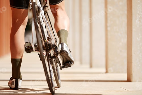 Preview: Close up, low angle view on a bike, back wheel on foreground. Man's legs riding his bicycle on road