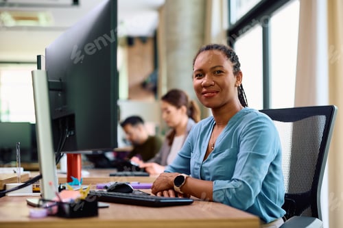 Preview: Happy black businesswoman working in the office and looking at camera.