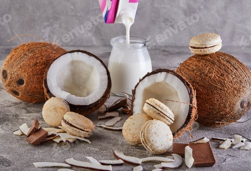Preview: Coconut macarons with chocolate and coconut flakes on a table with a coconut in the background