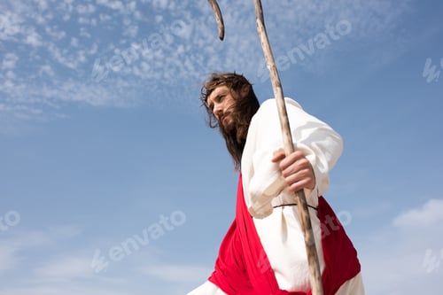 Preview: low angle view of Jesus in robe, red sash and crown of thorns standing with staff against cloudy sky