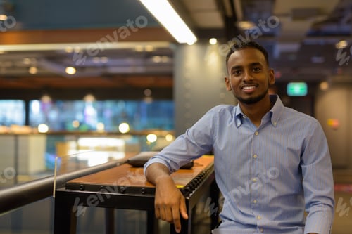 Preview: Portrait of handsome black African businessman sitting inside shopping mall while smiling