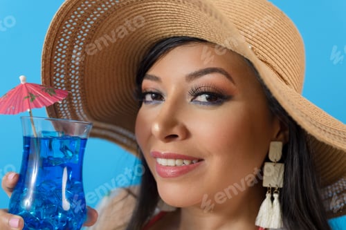 Vista previa: Primer plano de una mujer con sombrero para el sol sosteniendo un cóctel. Fondo azul.