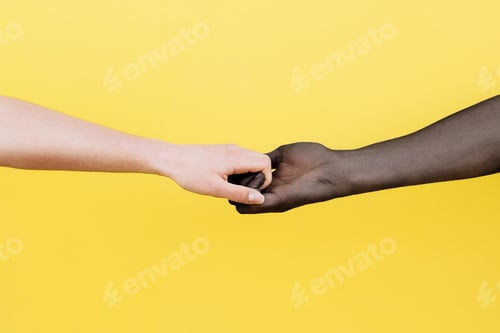 Preview: White hand and black hand clasped on yellow background