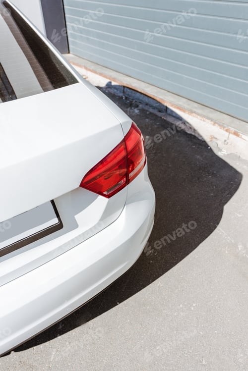 Preview: cropped image of red rear headlight on white car on street near garage