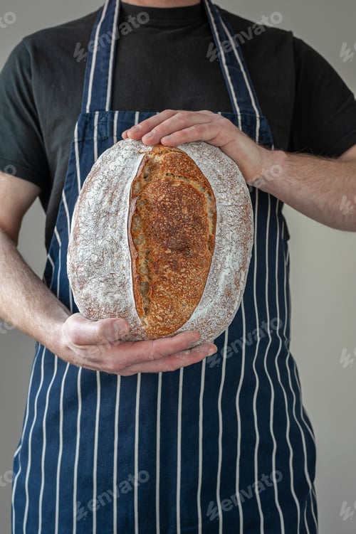 Preview: Close-up at bakers hands holding a loaf of bread in front of him.