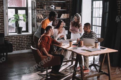 Preview: young, positive multicultural businesspeople brainstorming near desk in office