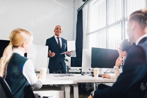 Preview: low angle view of smiling young african american businessman looking at coworkers in office