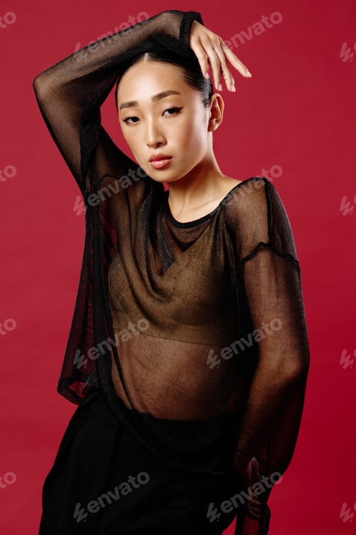 Preview: Fashion asian woman in a sheer top and black pants posing on a red background
