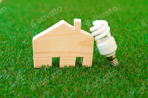 Preview: Wooden house model and lightbulb on green background