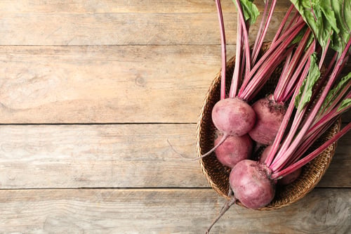 Preview: Raw ripe beets in wicker bowl on wooden table, top view. Space for text
