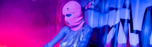 Preview: anonymous tattooed woman in balaclava near wall with graffiti in blue and pink lighting with smoke,