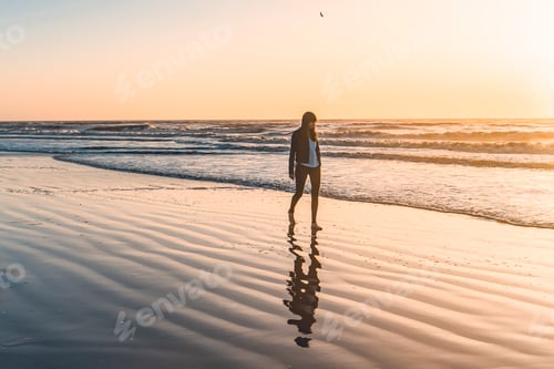 Preview: A lonely woman at the beach walking barefooted by the shore at sunrise.