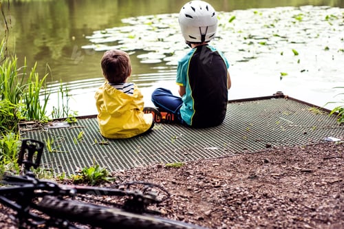 Preview: Two young brothers sitting at water's edge, rear view