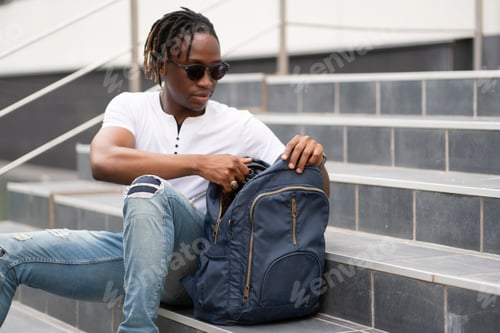 Preview: a male student opens his backpack and taking some things out of it in the city