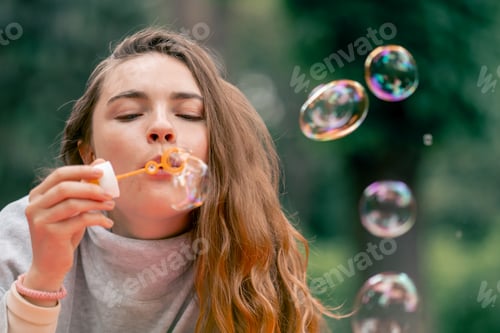 Preview: close up in the park in nature a young girl blows soap bubbles a return to childhood a huge bubble