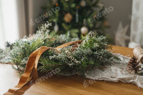 Preview: Making stylish Christmas rustic wreath. Wreath with evergreen branches, ribbon, scissors on table