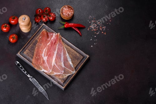 Preview: Italian prosciutto crudo or spanish jamon on a dark cutting board