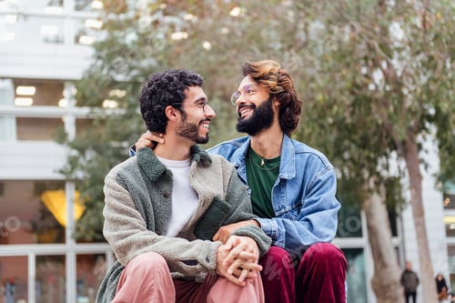 Preview: couple of gay men sitting in a park smiling happy