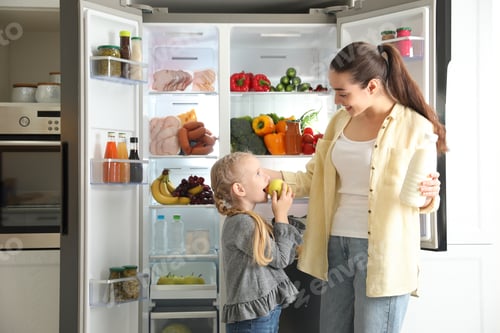 Preview: Young mother and her daughter with products near open refrigerator in kitchen