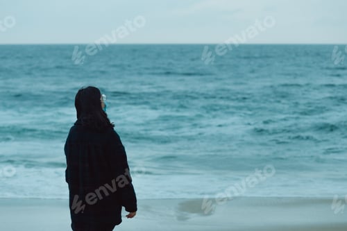 Preview: Woman giving the back to the camera in front of a massive ocean with copy space