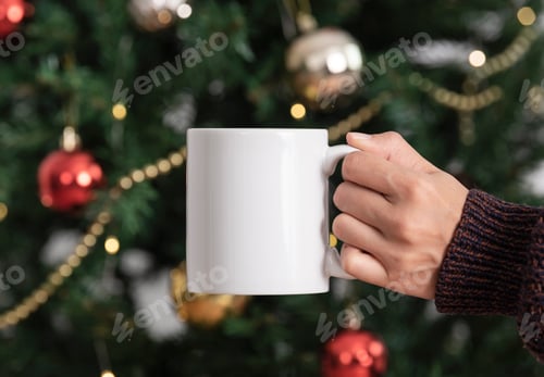 Preview: hand holding white ceramic coffee cup with christmas tree background. mockup mug