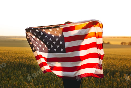 Preview: Beautiful girl with American flag in a wheat field at sunset