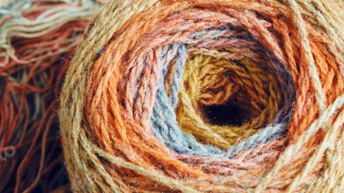 Preview: Ball of yarn from pure organic sheep's wool on an unwound skein of woolen threads. Rainbow color.