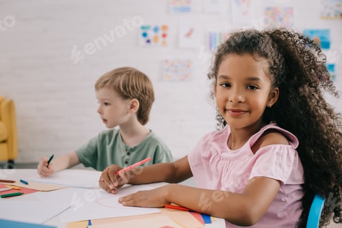 Preview: selective focus of multicultural preschoolers at table with papers and pencils in classroom