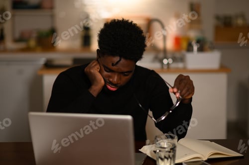 Preview: A multicultural man is sitting at home and sleeping in his working area on a table late at night.