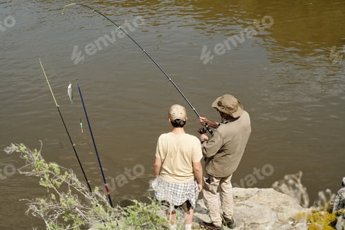 Preview: Middle Aged Man Teaching Young Boy Fishing Outdoors by Riverbank