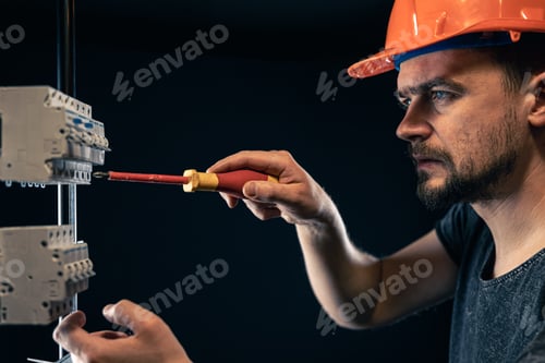 Preview: A male electrician works in a switchboard with an electrical connecting cable.