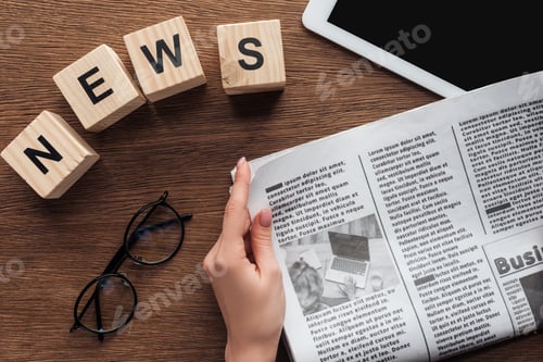 Preview: cropped image of journalist holding newspaper, wooden cubes with word news at wooden table