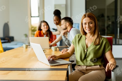 Preview: Business woman working on laptop with her young multiethnic startup team working in modern office