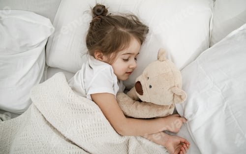 Preview: A cute little girl is sleeping in a bed with a Teddy bear toy .