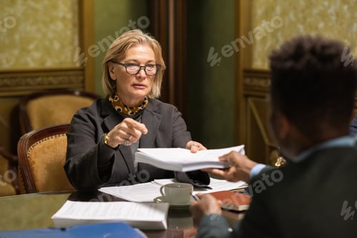 Preview: Mature businesswoman passing stack of signed documents to colleague
