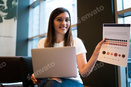 Preview: happy female designer holdin infographic paper happy about completing project on laptop